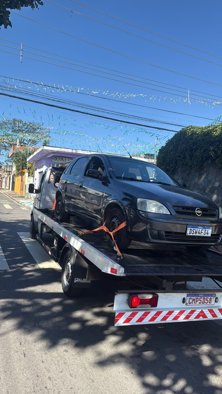 Caminhão plataforma da AL Guinchos transportando veículo de dia